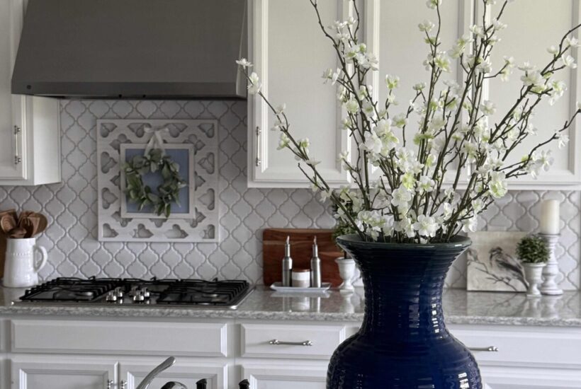 A tall blue vase filled with flowering branches sits on a kitchen counter.