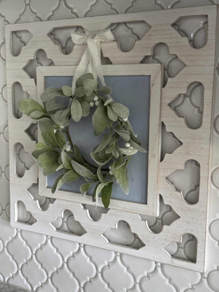 Spring kitchen decor idea #1 is to hang a lamb's ear wreath with a white ribbon, over a white frame with a blue background.