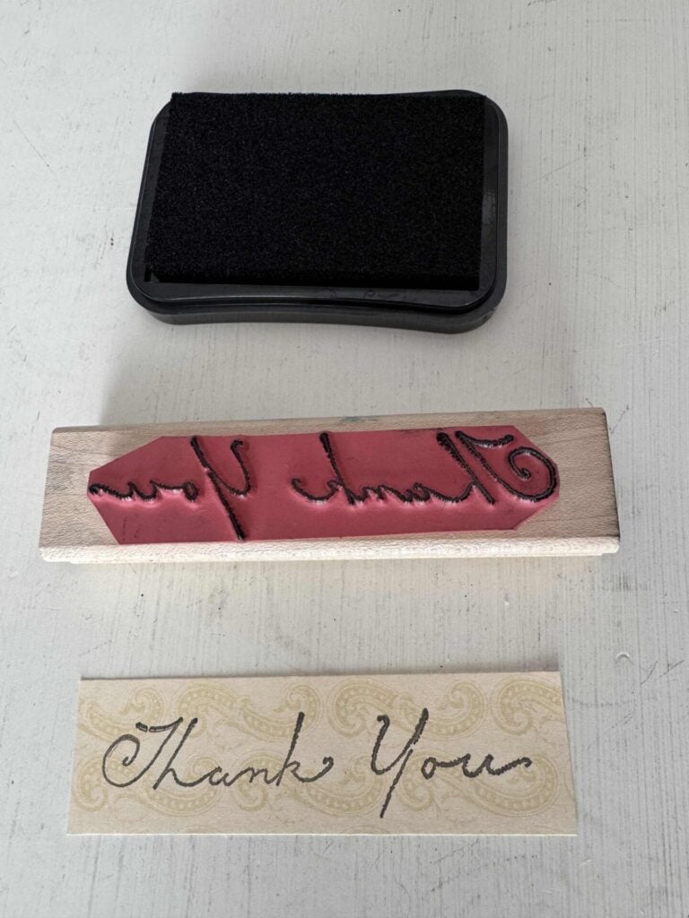 A black ink pad, A "thank you" stamp, and a piece of paper with the words stamped on it.