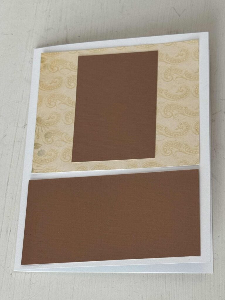 A white card with a piece of patterned cardstock and a brown rectangle on top of it and another brown rectangle below.  