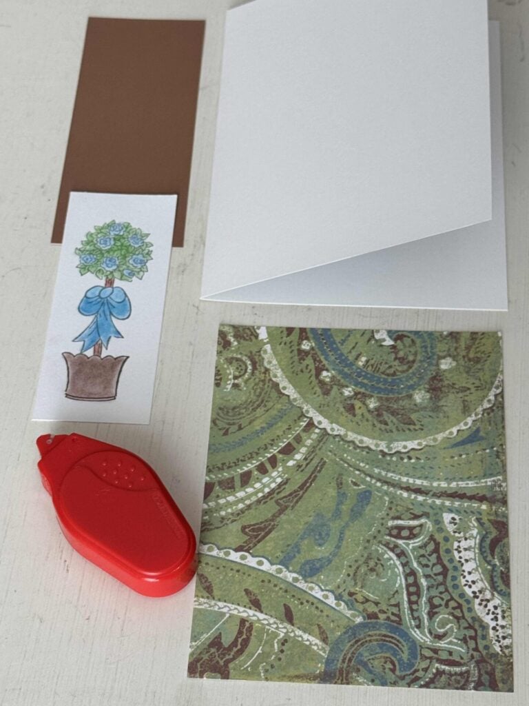 A blank white card with a topiary stamp, cardstock, and a tape runner. 