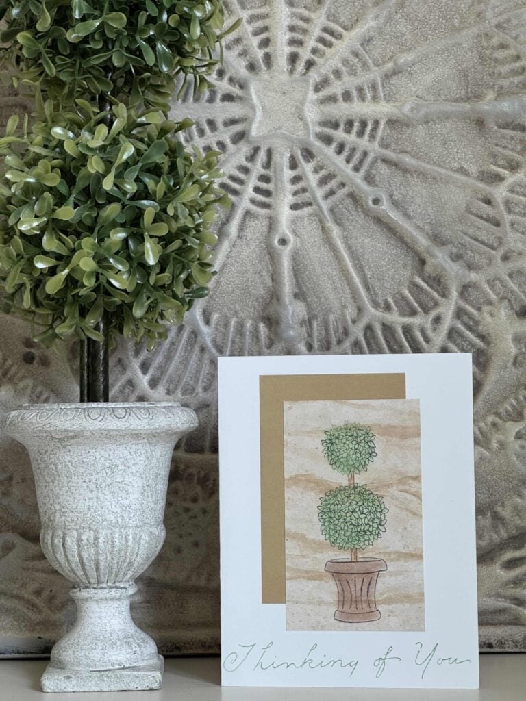 A handmade card that says "thinking of you" sitting next to a faux topiary. 