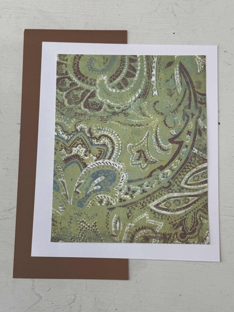 A piece of patterned cardstock laying on a piece of white cardstock and a piece of brown.