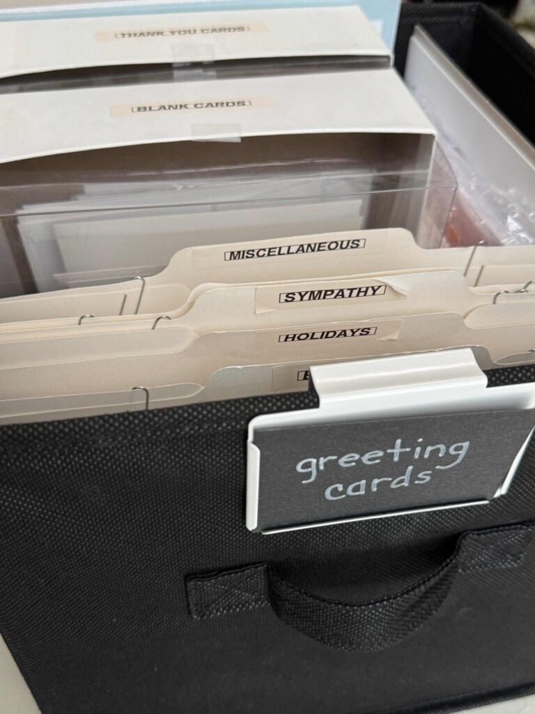 A black storage bin labeled greeting cards helps organize greeting cards with dividers for THANK YOU, BLANK, MISCELLANEOUS, SYMPATHY, and HOLIDAYS.