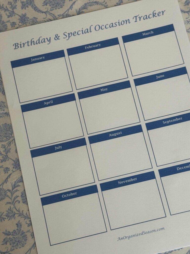 A blank “Birthday & Special Occasion Tracker” sheet with 12 labeled boxes for each month, perfect to organize greeting cards and important dates. The sheet rests on a blue and white floral-patterned surface.