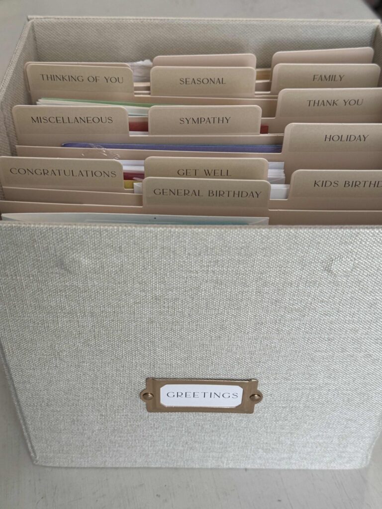A fabric-covered box to organize greeting cards, featuring labeled dividers for occasions like Congratulations, Get Well, Sympathy, Thank You, Holiday, and more. The box label reads GREETINGS.