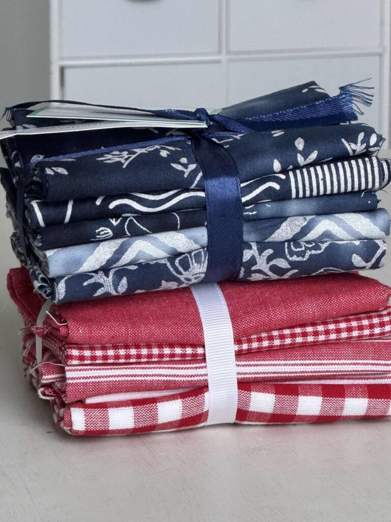Two neatly folded stacks of fabric are tied with ribbons; the top stack features various blue and white patterns, while the bottom stack has red and white checkered and striped designs.