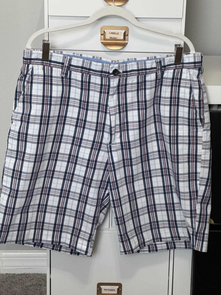 A pair of plaid shorts with a pattern of blue, black, and red lines on a white background hangs on a hanger in front of a dresser, adding a touch of style perfect for pairing with your next DIY Fabric Orbs project.