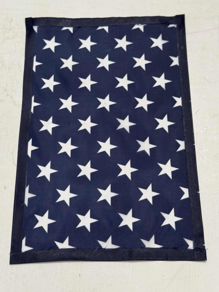 A rectangular piece of dark blue fabric with evenly spaced white stars and a solid dark border, laid flat on a light-colored surface.