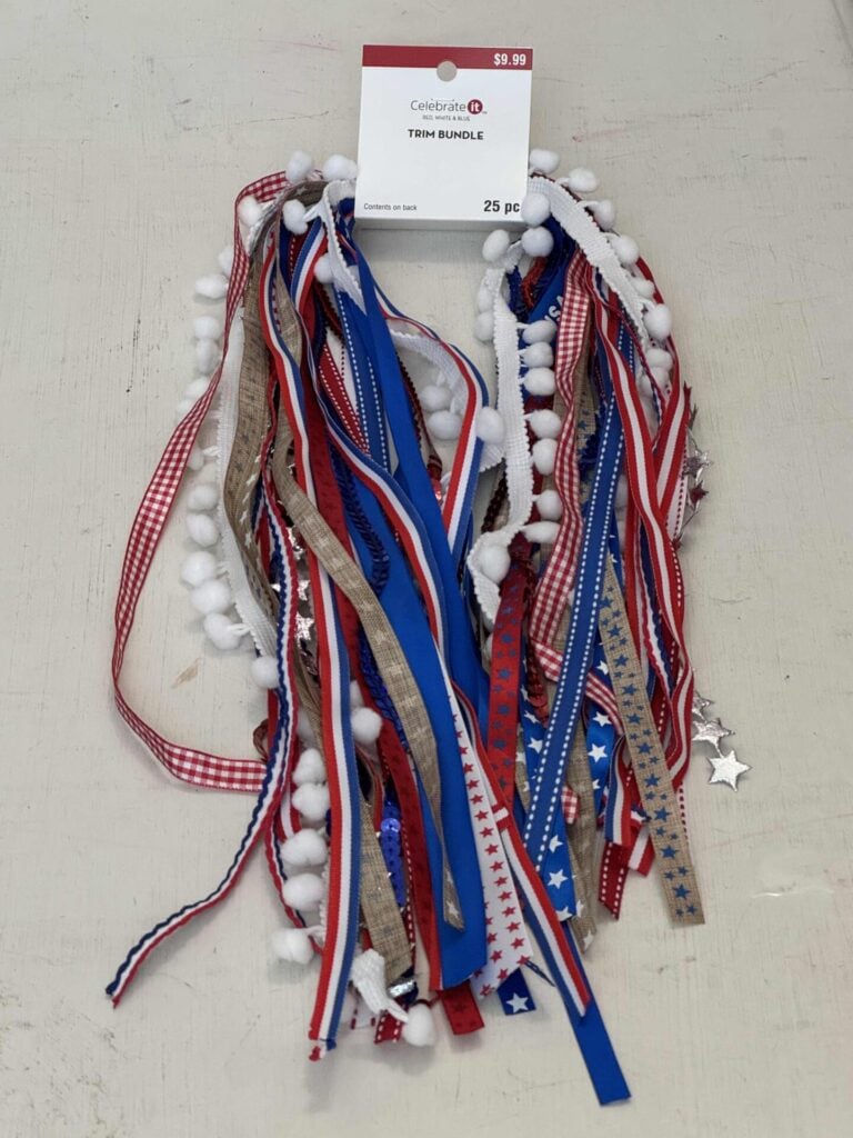 A bundle of assorted red, white, and blue ribbons with stars, stripes, and pom-poms. Labeled “Trim Bundle” by Celebrate It, priced at $9.99 and contains 25 pieces.