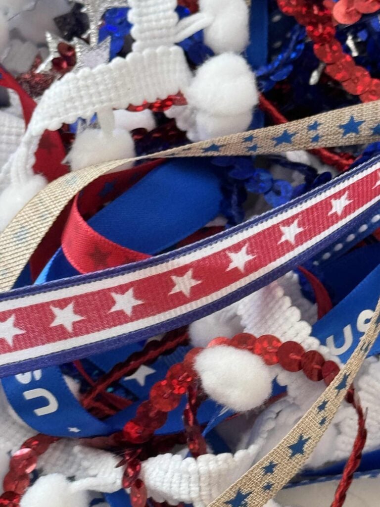 A colorful mix of patriotic ribbons and decorations in red, white, and blue, featuring stars, sequins, and pom-poms.