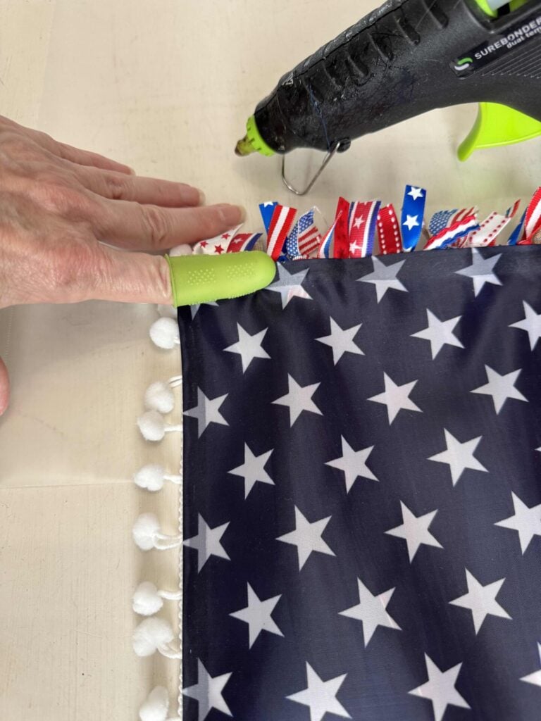 A hand with green finger protectors presses navy blue fabric with white stars, onto a ribbon flag.