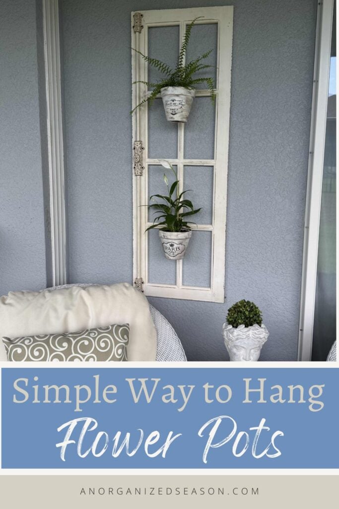 A white window frame holds two small flower pots with green ferns, hanging on a gray wall above a white chair with a pillow. Text reads: Simple Way to Hang Flower Pots—discover how to hang flower pots easily and beautifully in your home décor.