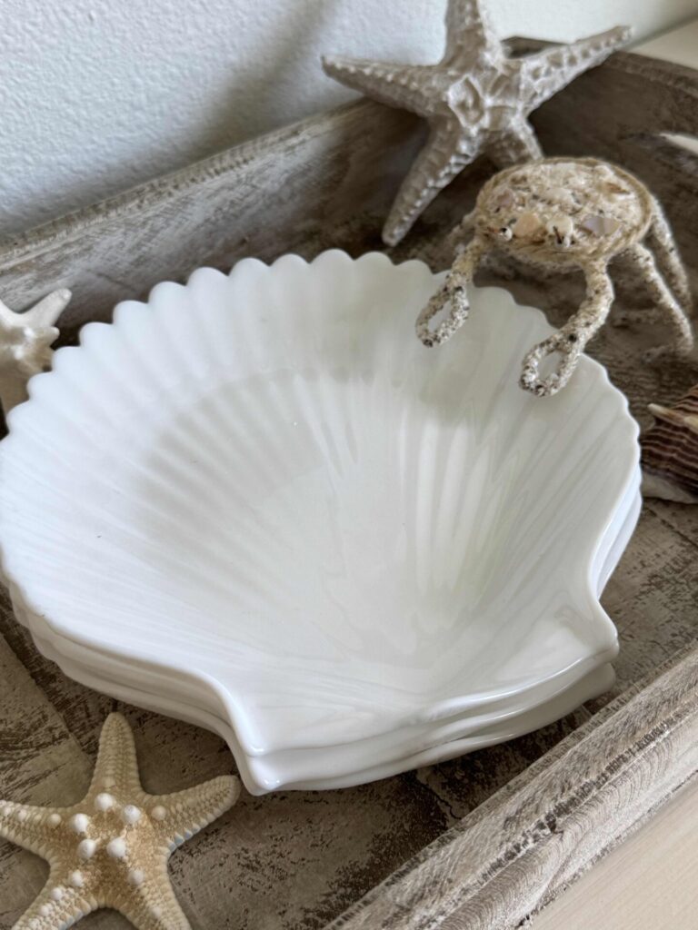 A white ceramic shell-shaped dish sits in a rustic wooden tray, surrounded by decorative starfish and a small crab figurine, making it a charming addition to your Summer Decor Ideas.