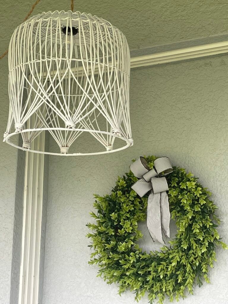 A white wire pendant light and a green wreath with a black-and-white striped bow hang on a light gray textured wall, offering inspiration for stylish décor arrangements and clever ideas, much like those found in guides on how to hang flower pots.