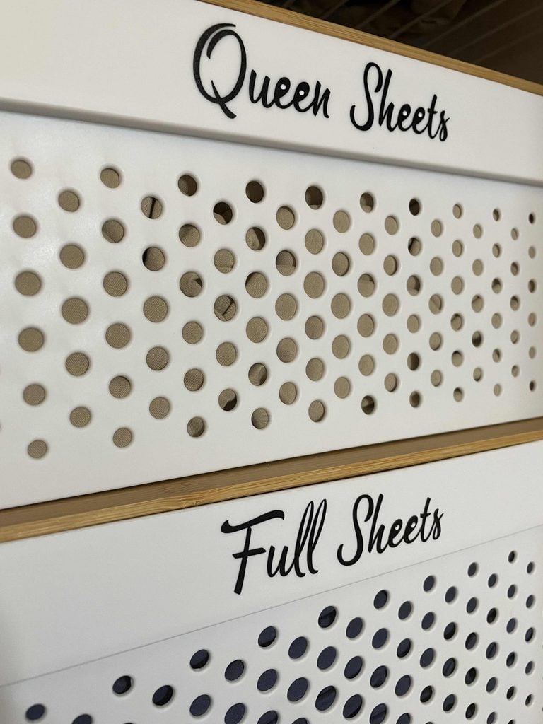 A store shelf labeled Queen Sheets above Full Sheets, both with decorative perforated panels, showcases elegant home organization products.