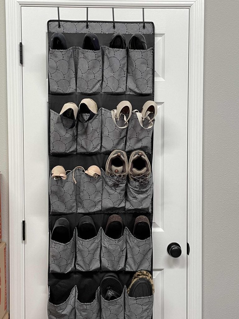 An over-the-door hanging organizer, one of the must-have home organization products, features multiple pockets holding various pairs of shoes and is attached to a white door with a black handle.