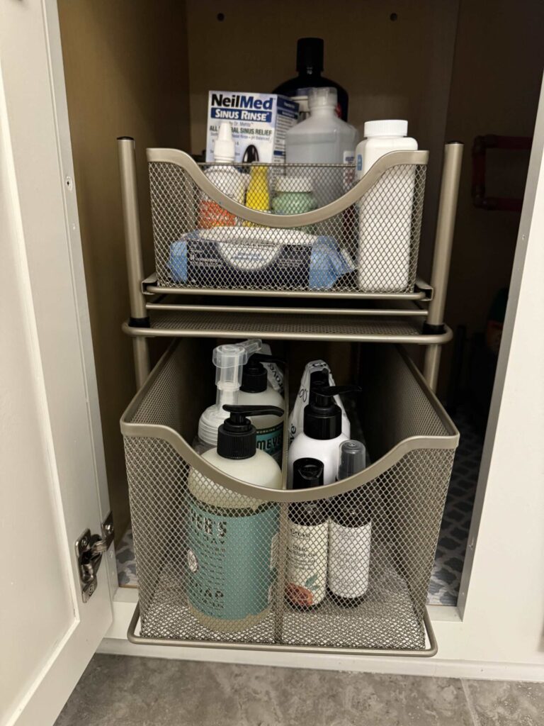 Two metal mesh drawers under a cabinet hold bottles, nasal rinse, and hygiene products, organized neatly for easy access. These home organization products feature sliding drawers for added convenience.