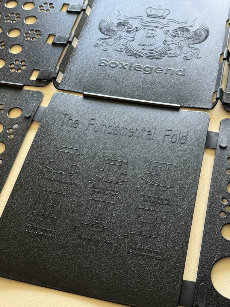 A close-up of a black plastic folding board labeled Boxlegend with an embossed crest, this staple among home organization products features instructions titled The Fundamental Fold and includes folding shirt diagrams.