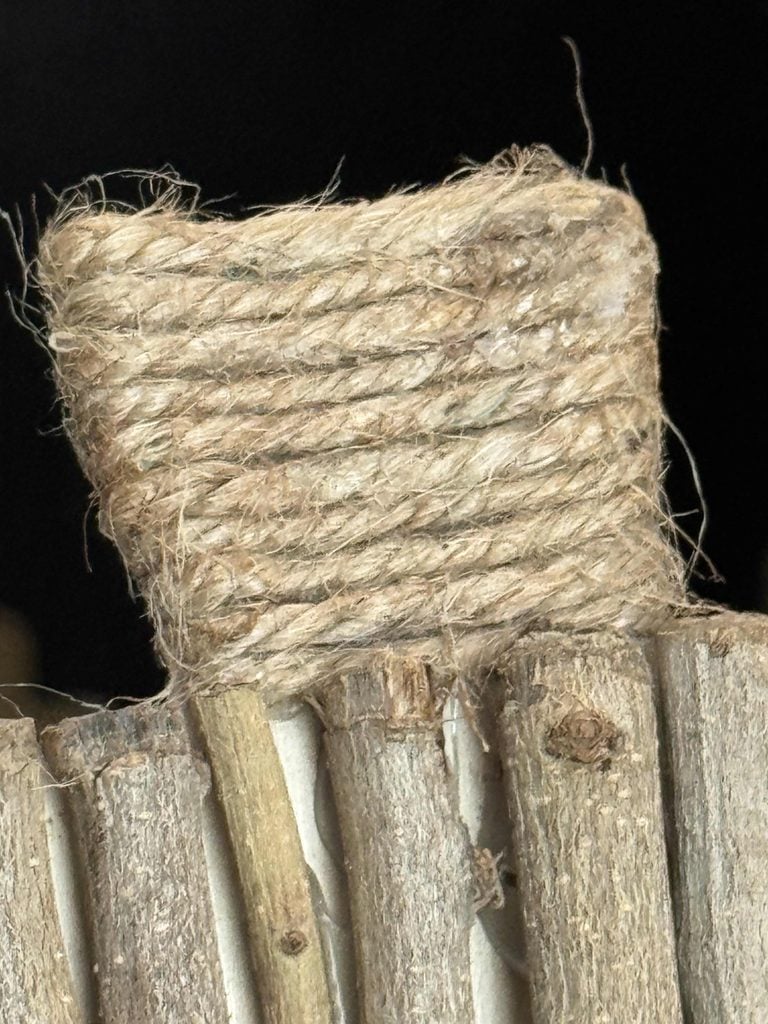 A close-up of a bundle of twine wrapped around a square object, resting on vertically arranged wooden sticks, with a dark background—perfect inspiration for your next DIY Twig Pumpkin project.