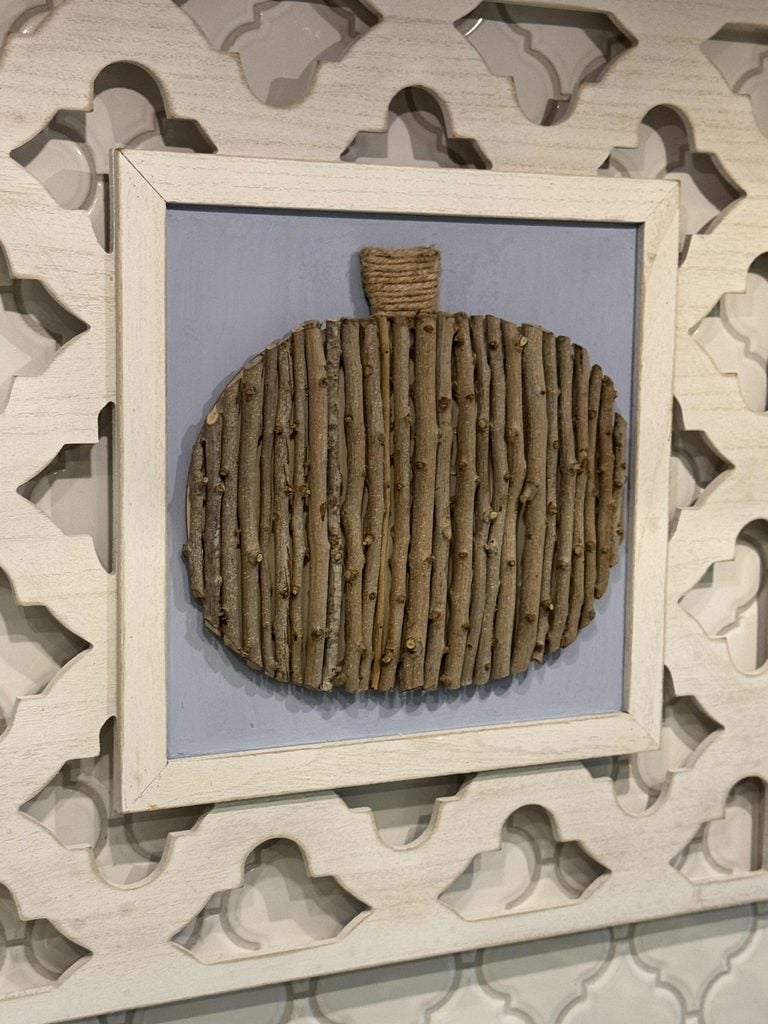 Wall art featuring a pumpkin shape made from vertical sticks, with a twine-wrapped stem, mounted on a light background and framed in white. A decorative cutout pattern surrounds the framed piece, evoking Seasonal Sentiments perfect for September 2026 Rewind.