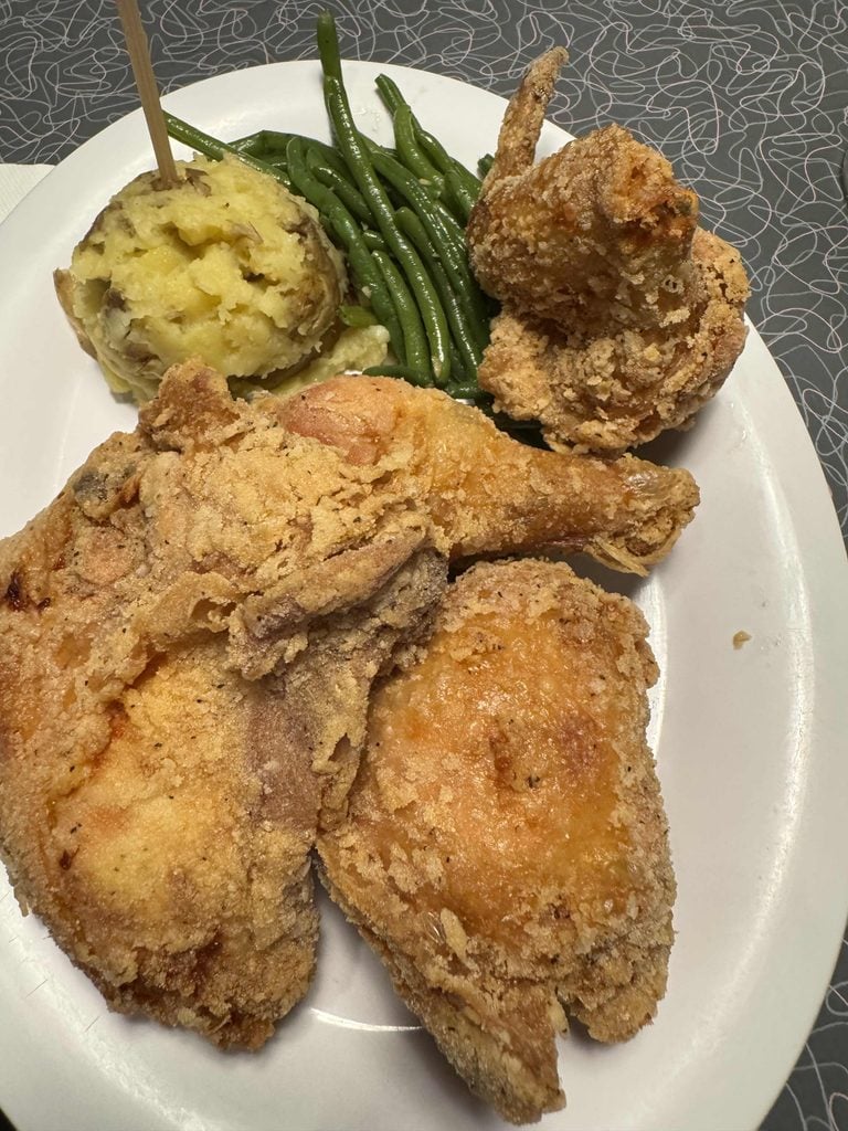 A plate with three pieces of fried chicken, a serving of green beans, and a scoop of mashed potatoes on a white plate.