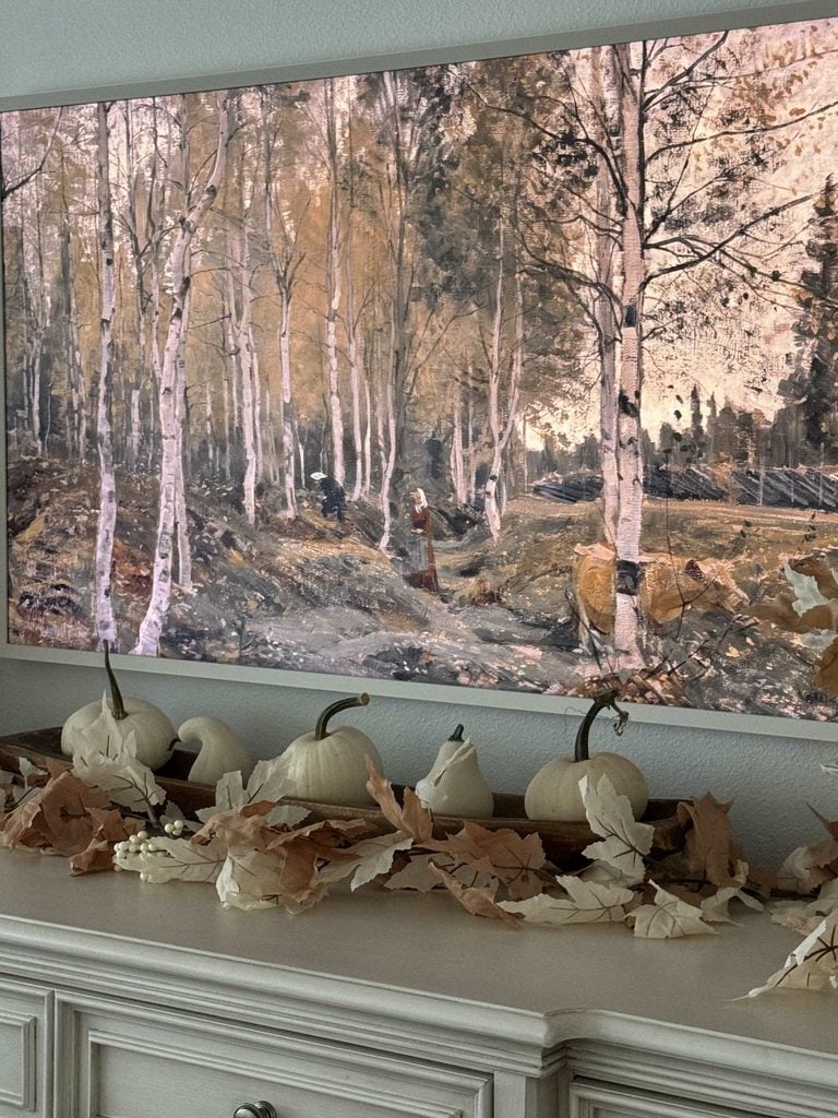 A painting of a birch forest hangs above a mantle decorated with white pumpkins, dried leaves, and garlands—showcasing one of the best natural fall decor ideas for creating a cozy autumn theme.
