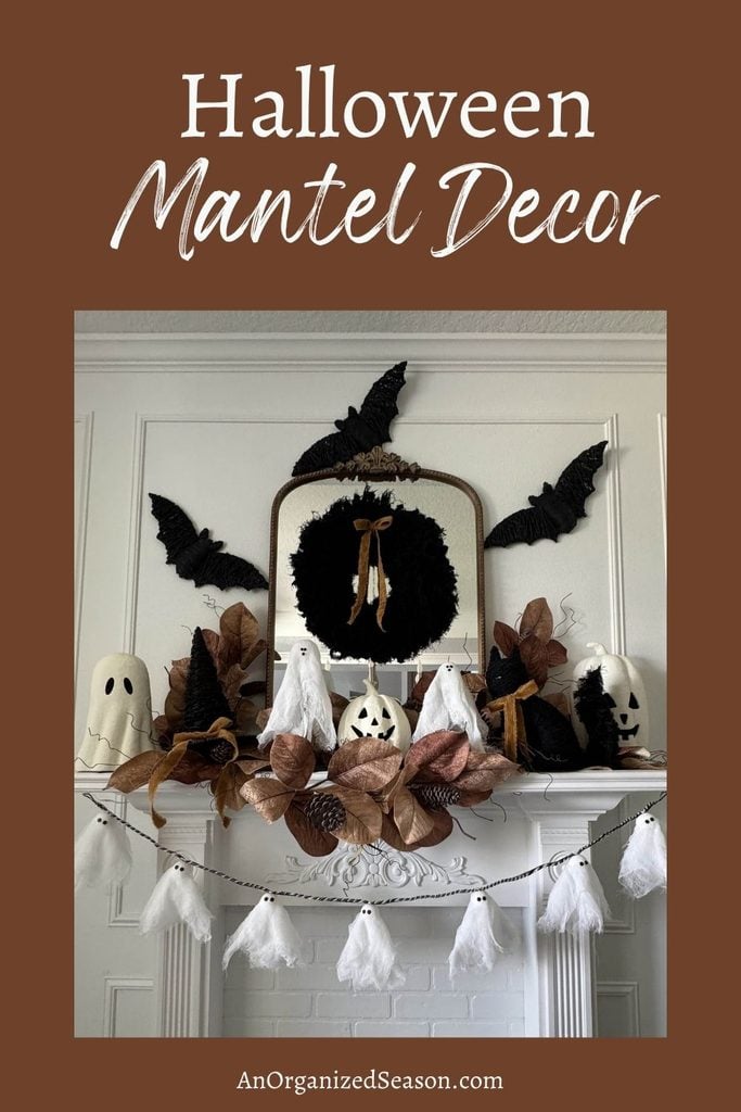 A white mantel styled with faux bats, ghosts, black and brown leaves, witch hats, and a black wreath under a mirror. Text reads Halloween Mantel Decor—perfect inspiration for your own Halloween mantel decor.