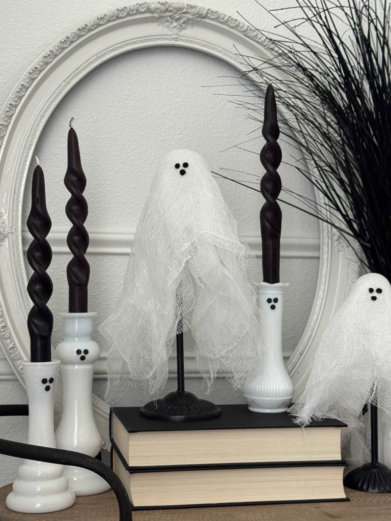 Halloween tabletop decor featuring two fabric-covered ghost figurines on stands alongside black spiral taper candles in ghost-faced holders, perfect for styling near a DIY ghost garland.
